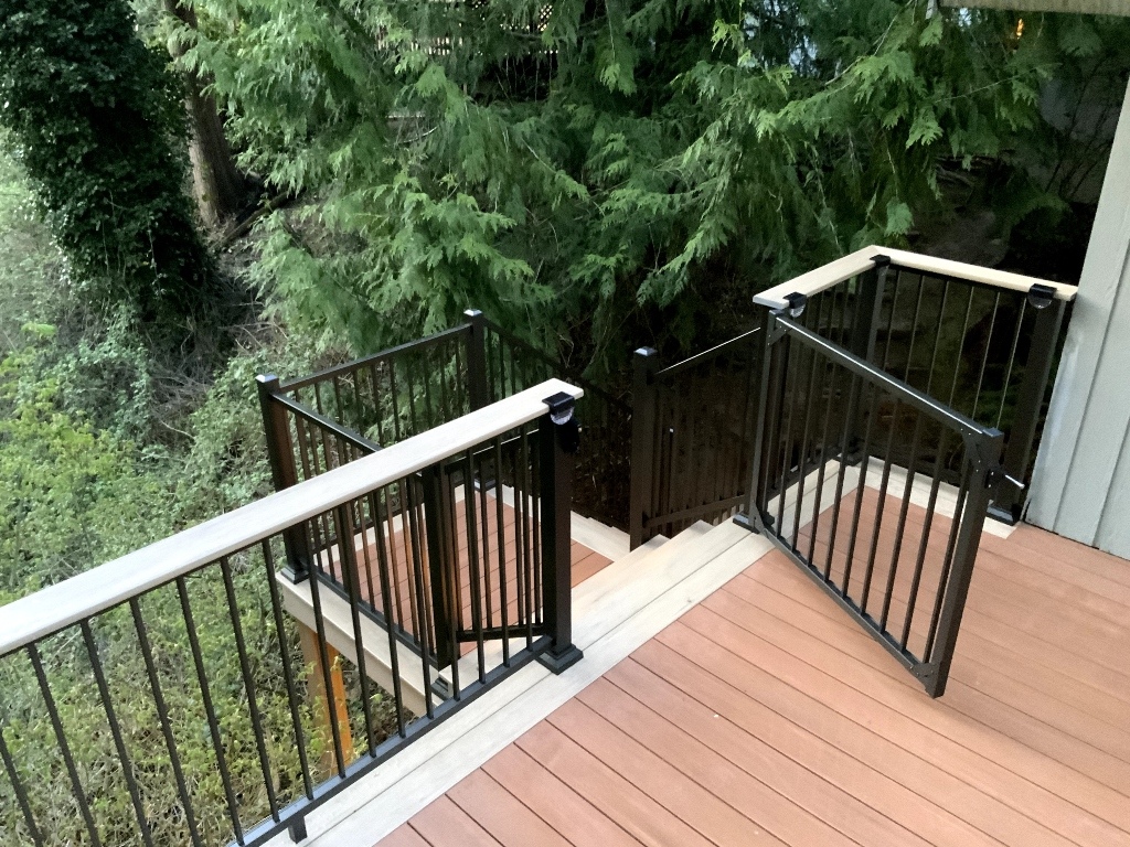 Composite deck with black aluminum railing and a gate to the stairs, surrounded by evergreens