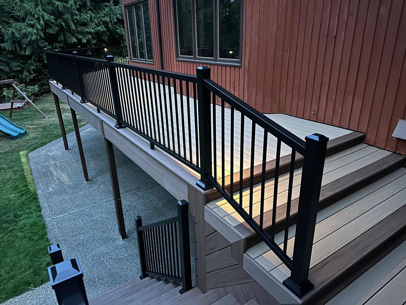 Elevated composite deck with black railing and stairs on a red cedar-sided home
