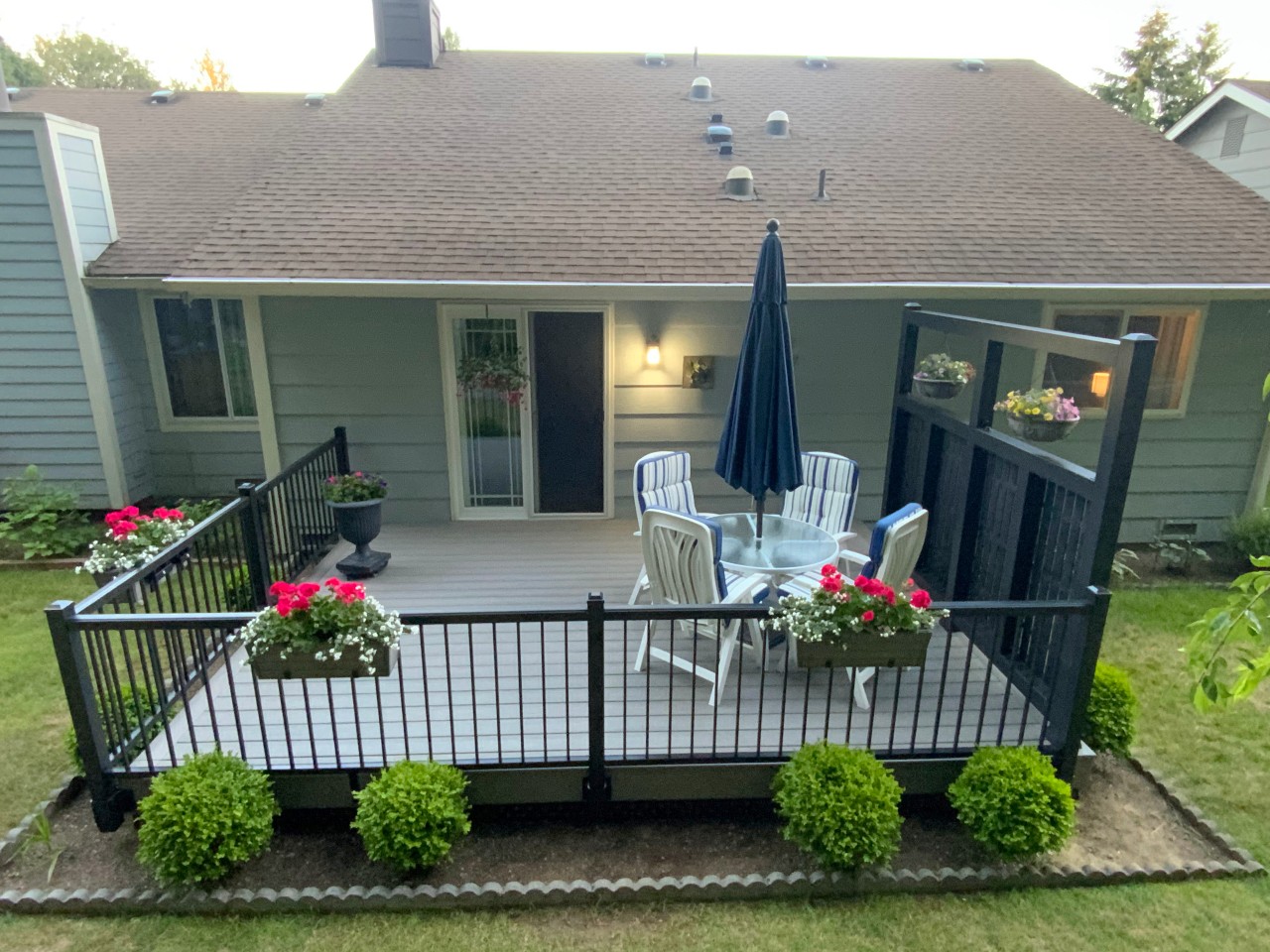 Small composite deck with black railing and flower boxes on a tan home