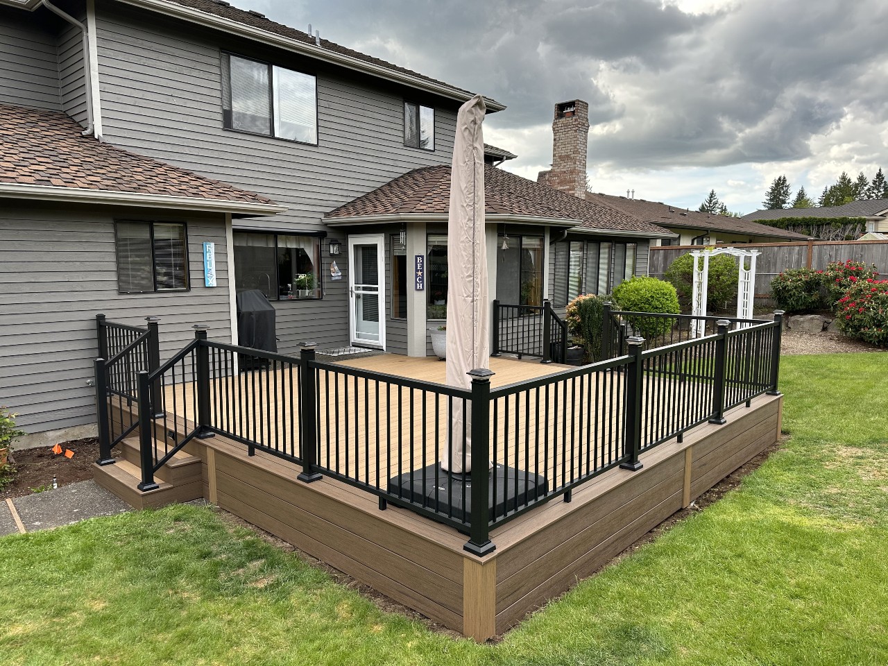 Composite deck with black aluminum railing on a grey home with a lawn