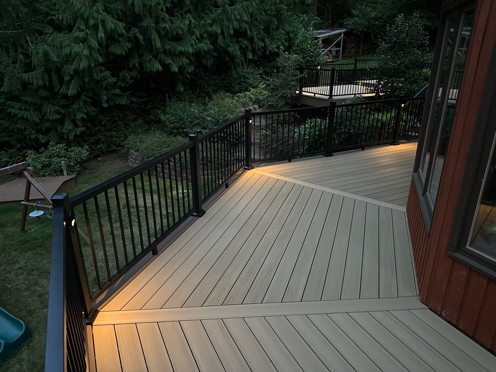 Composite deck with picture-frame border and black railing lit at dusk