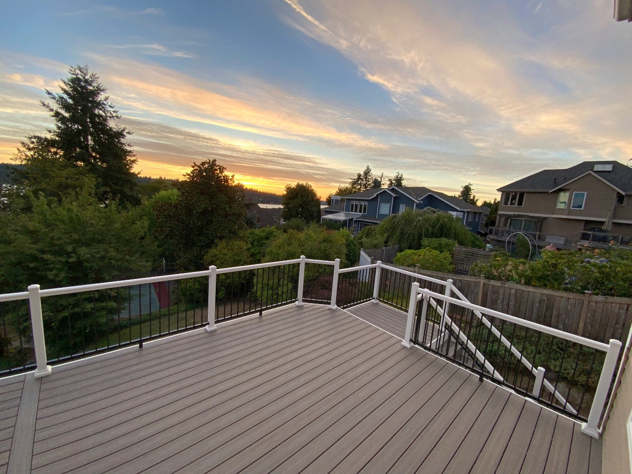 Wraparound composite deck with white posts and black balusters at sunset