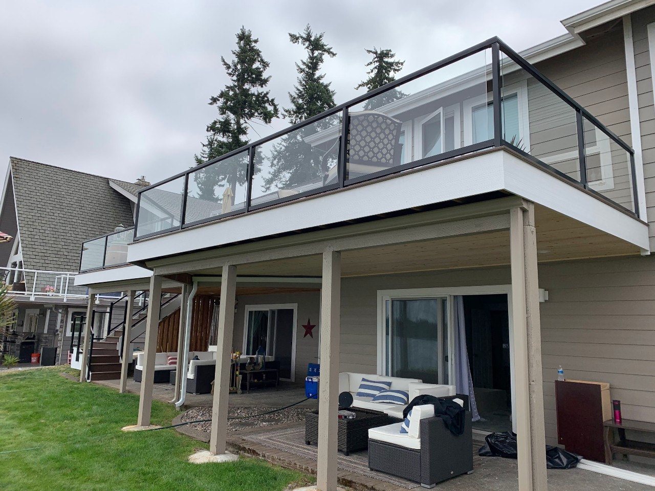 Two-story grey home with a glass-railing upper deck and covered patio below