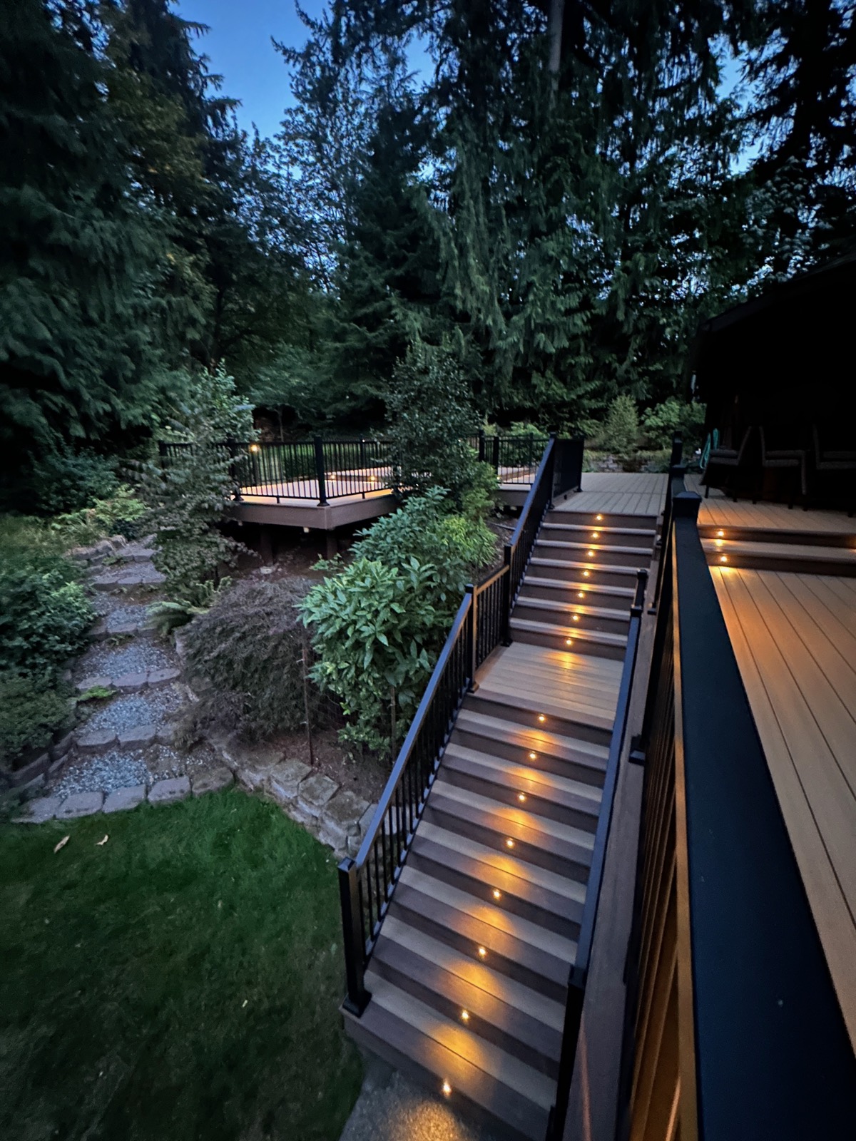 Lit composite stairs leading down a hillside to a lower deck at dusk