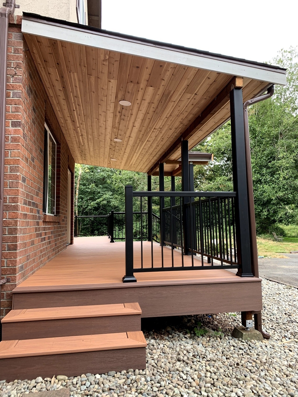 Covered front porch deck with tongue-and-groove ceiling and black railing on a brick home