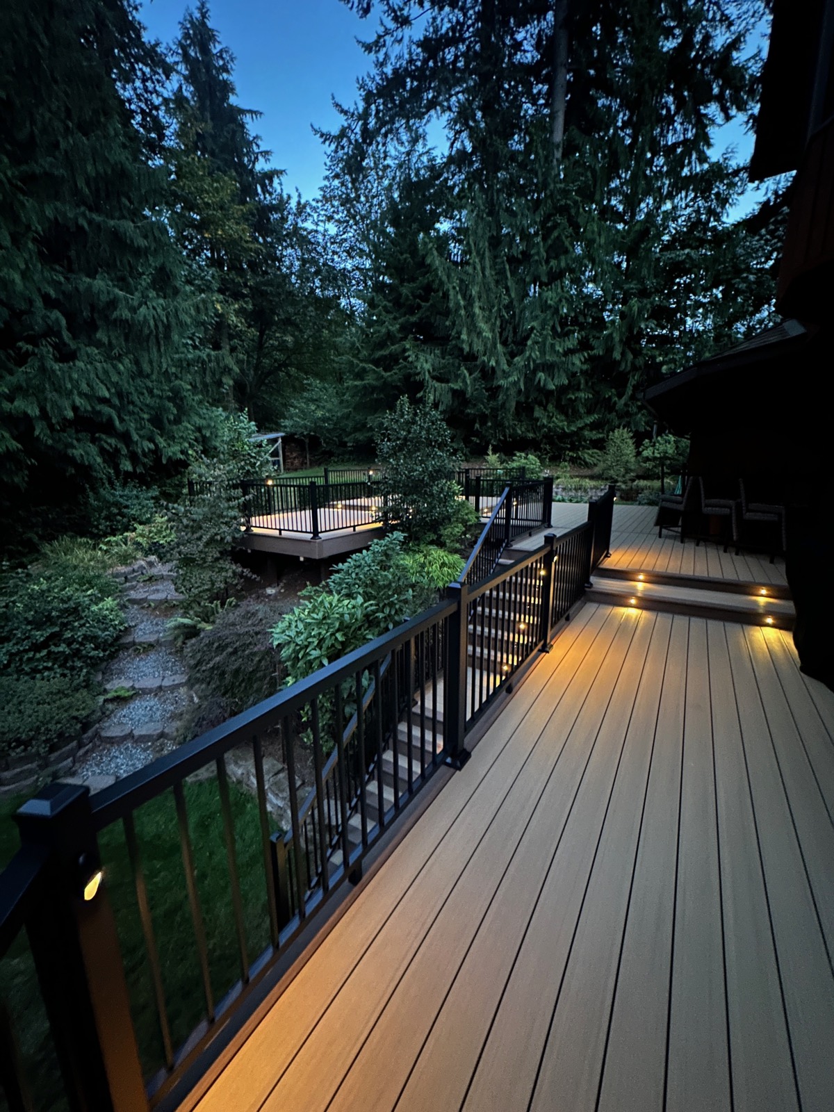 Multi-level composite deck with black railing and stair lighting at dusk