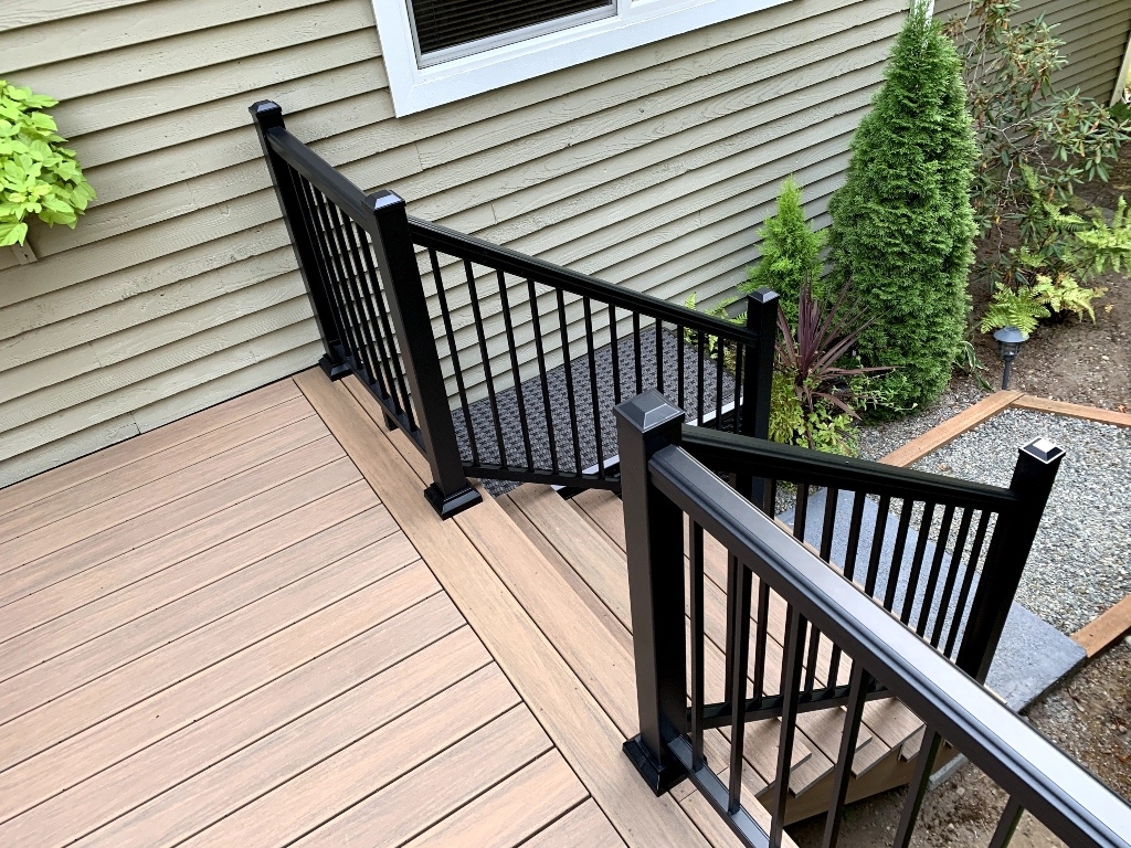 Composite deck with black aluminum railing and stairs beside evergreens
