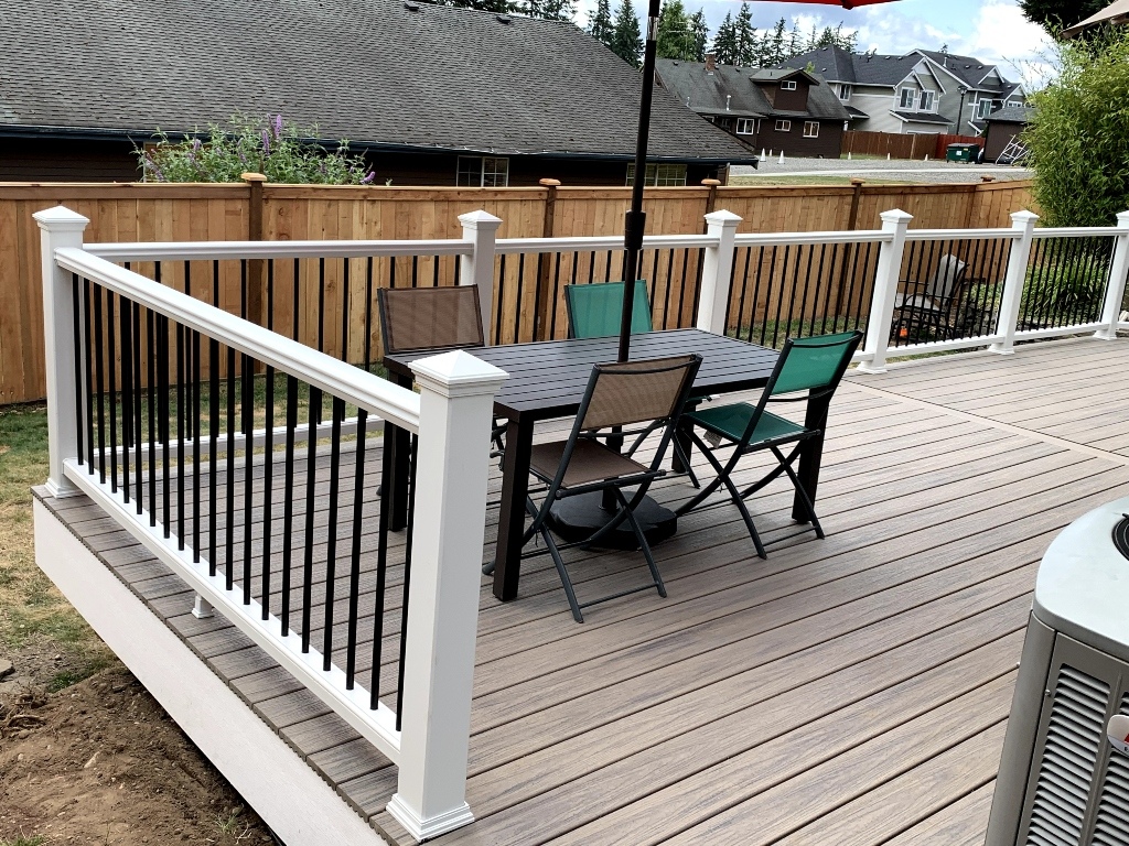 Composite deck with white railing and a dining set beside a cedar privacy fence