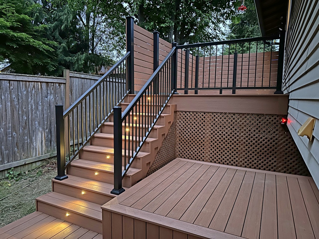 Multi-level composite deck with black railing and cedar privacy fence