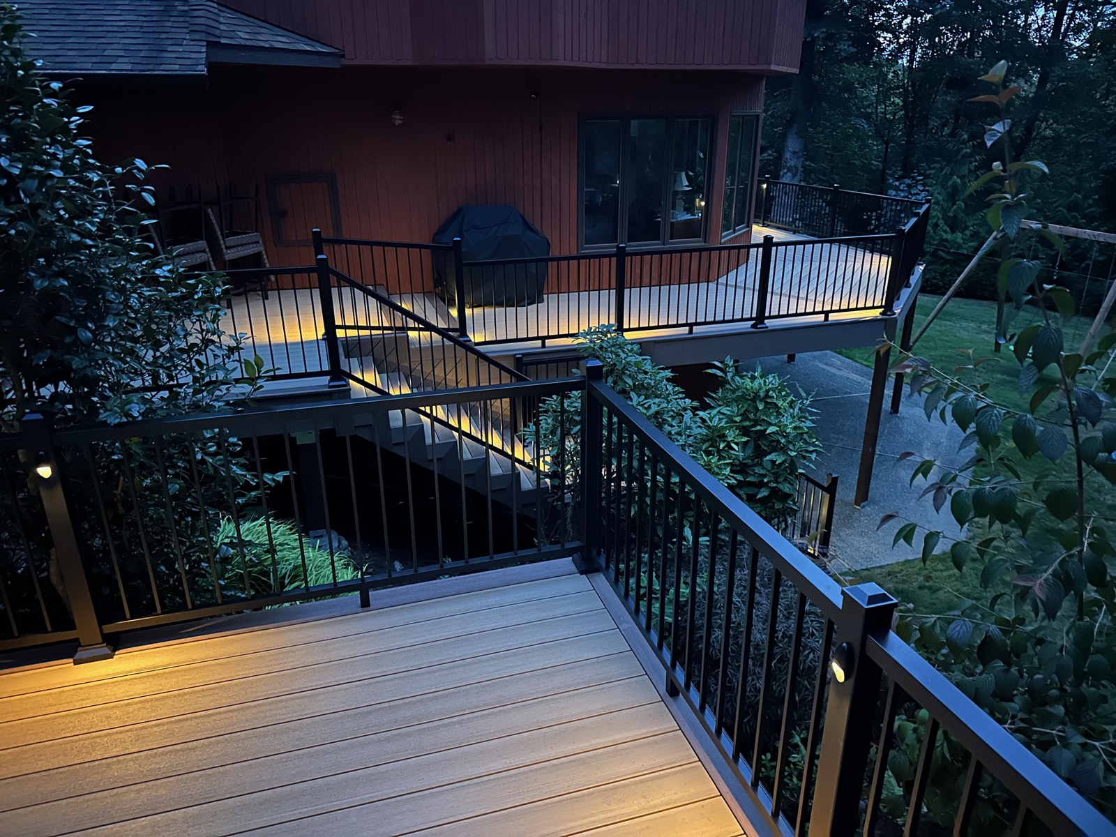 Two-level composite deck with railing lights on a wooded lot at night