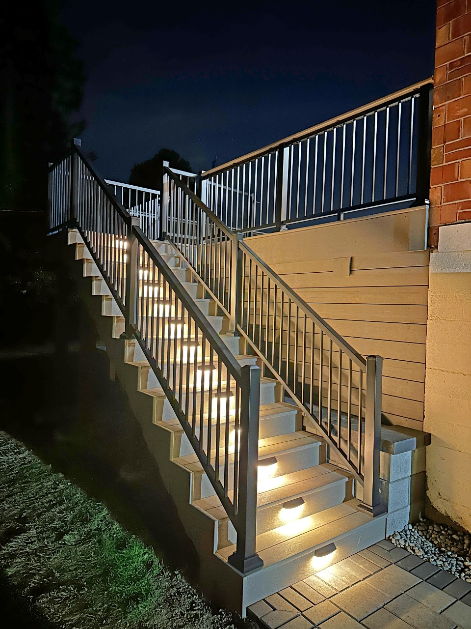 Lit composite stairs with black aluminum railing at night