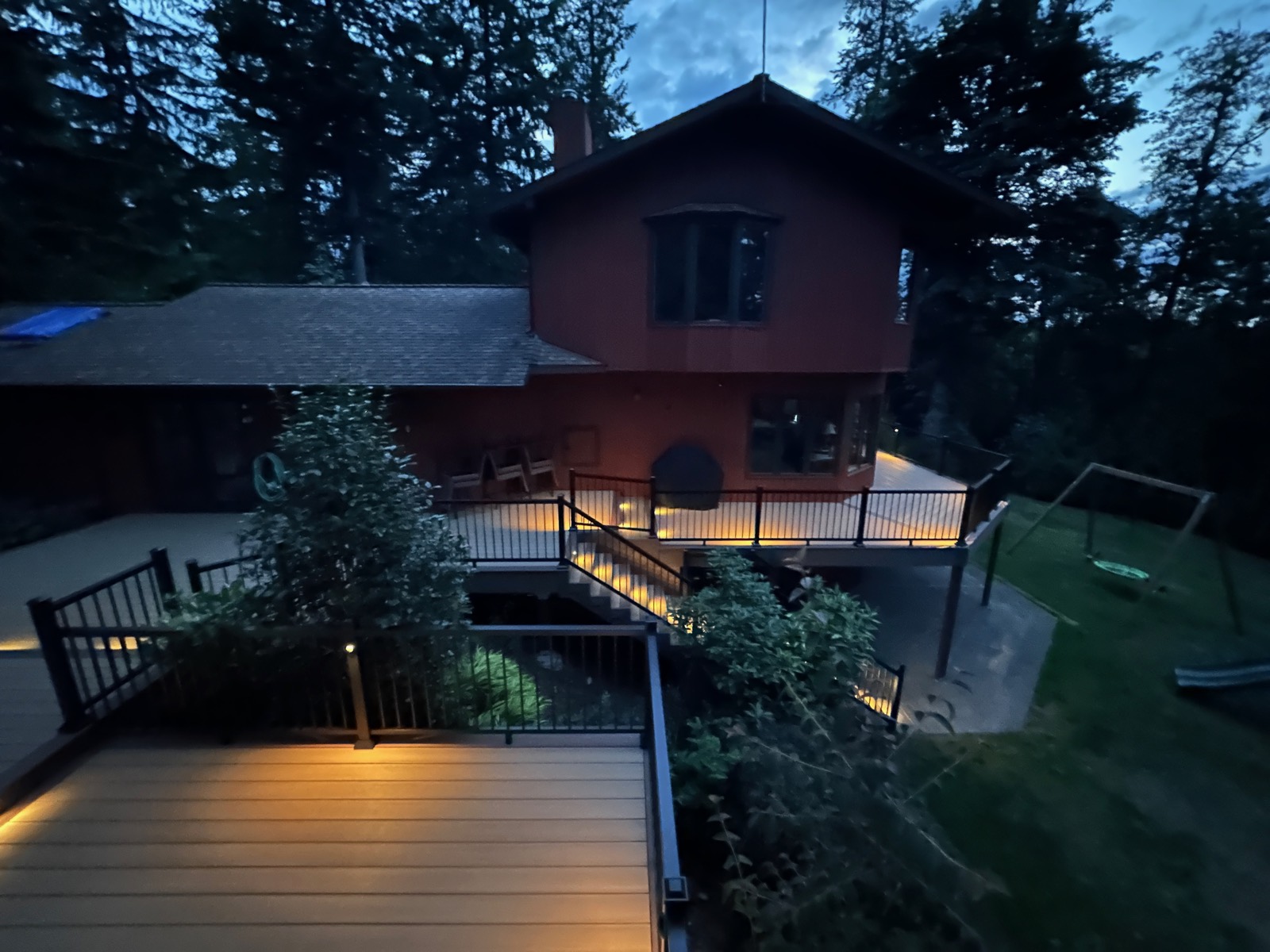Red two-story home with a new lit composite deck and stairs at night