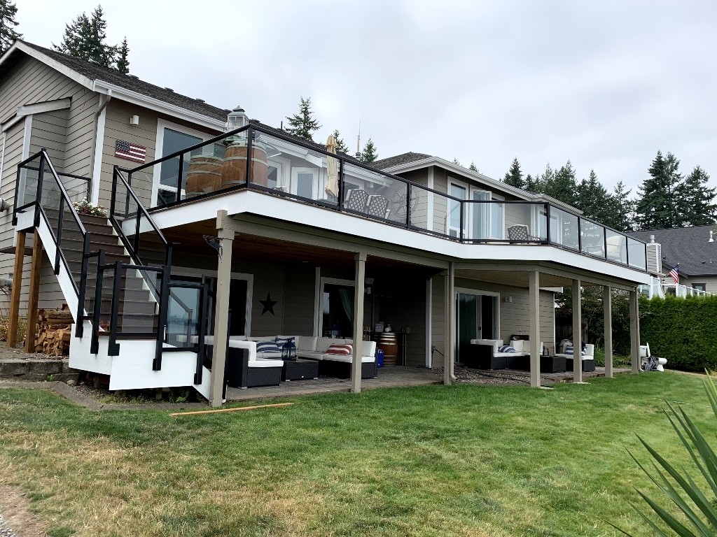 Long second-story composite deck with glass railing above a covered patio