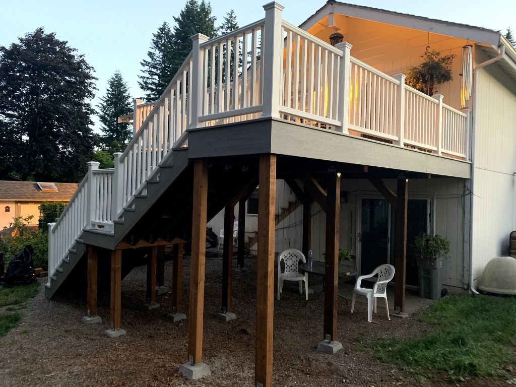 Second-story composite deck with white railing and stairs above a patio