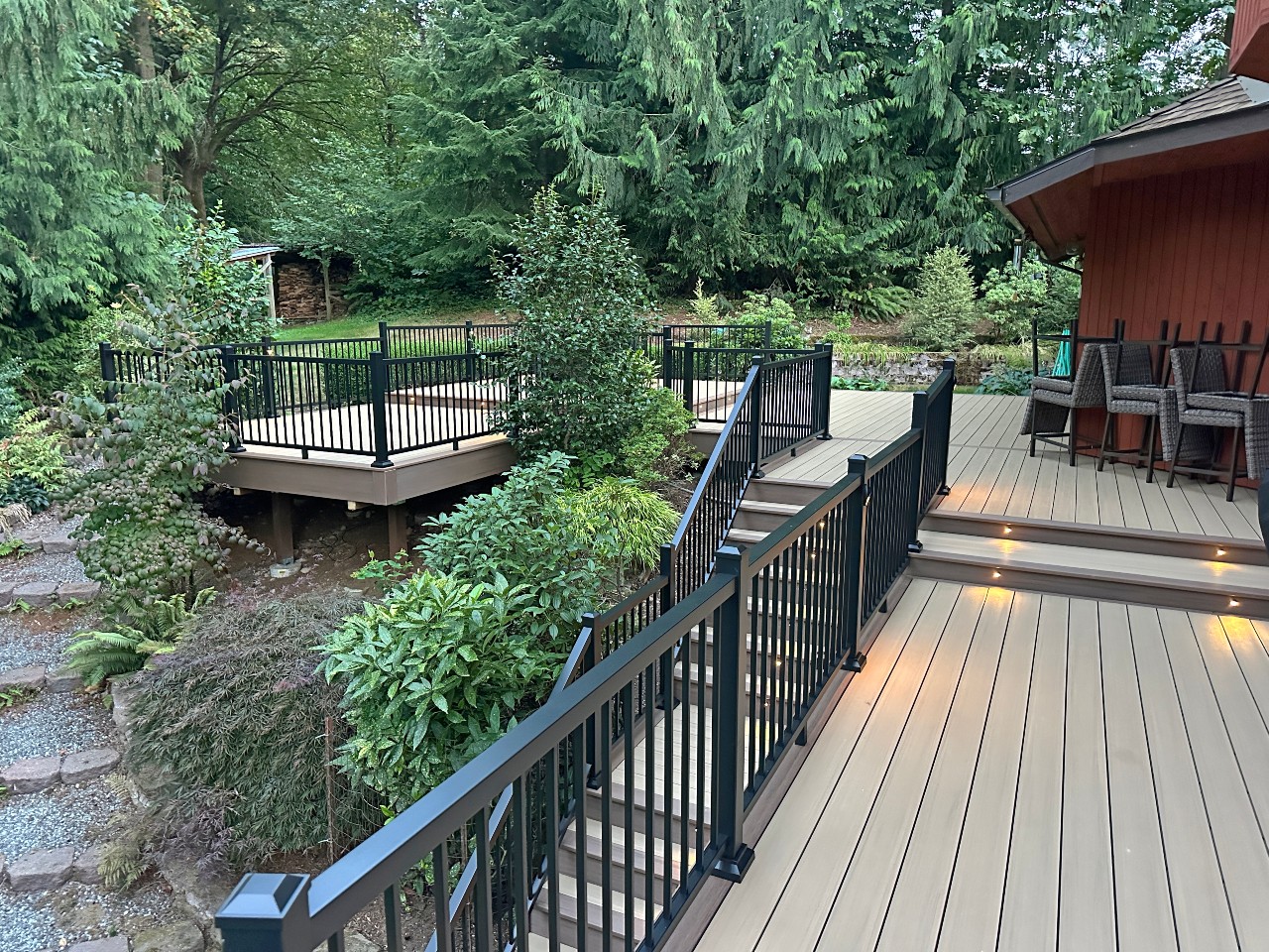 Composite deck with black railing and step lighting beside a wooded yard