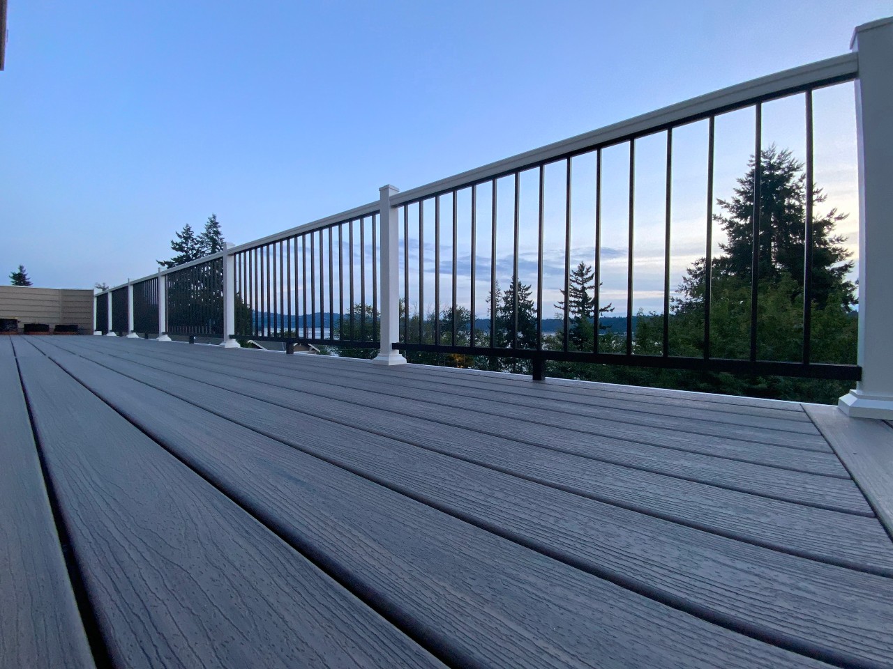 Grey composite decking with black aluminum railing under an evening sky